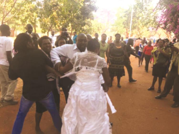 Francisca Kanyama (in wedding dress) is shielded by a Good Samaritan from battering by an irate Magdalene Chamunorwa (partly obscured) outside the Harare Magistrates’ Courts yesterday