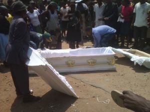 People watching relatives putting the corpse back into the casket which fell from the car when people who were holding it fled after the arrival of the police in Mbare 