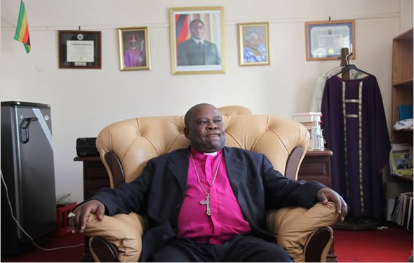 Bishop from Hell: Nolbert Kunonga in his Harare offices with a picture of Robert Mugabe in the background