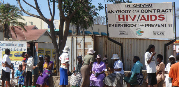 People sitting by an HIV/AIDS awareness sign in Zimbabwe