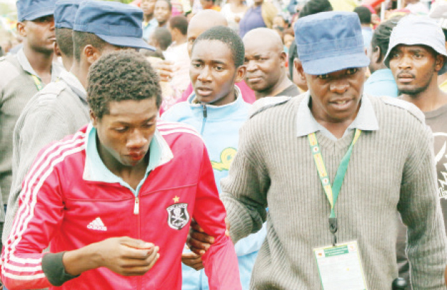 File Picture: A police officer escorts a man who was injured during a fight at the Soweto end of Barbourfields Stadium during the Region 5 Under-20 Youth Games closing ceremony in Bulawayo on Sunday