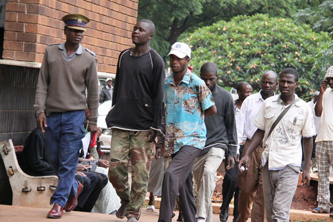 Police escort a robbery suspect in tattered Zimbabwe National Army fatigues to court in Harare in this file picture