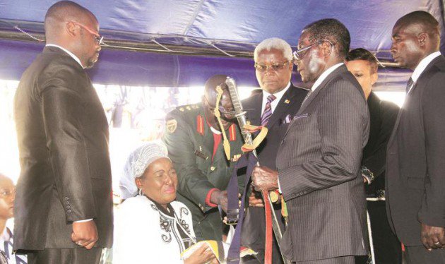 President Mugabe hands over a flag and a sword to Mrs Tapuwa Muchemwa, widow of national hero Retired Brigadier-General Felix Muchemwa, while son Fungai (left) and Home Affairs Minister Dr Ignatius Chombo (standing next to the President) look on at the National Heroes Acre in Harare yesterday. (Picture by Munyaradzi Chamalimba)