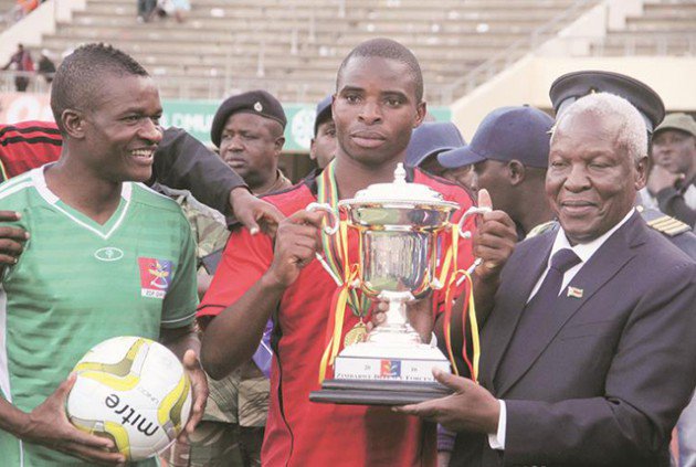 THE WINNERS TAKE IT ALL . . . Defence Forces Minister Sydney Sekeramayi hands over the Defence Forces Trophy to Zimbabwe Defence Forces Select skipper Bruce Homora (centre) while Phillip Marufu looks on after their victory over CAPS United at the National Sports Stadium yesterday
