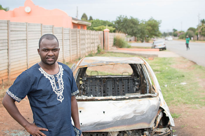 Patson Dzamara near the shell of his burnt out car