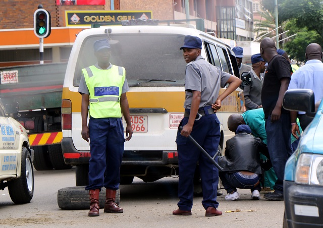File Picture: Riot Police was called in to cool public temper after traffic Police officers threw a spike on Tshova Mubaiwa commuter omnibus at the intersection of Hebert Chitepo and 9th Avenue, Bulawayo. In the picture, the driver of the Kombi changes the punctured tyre while the officers guard.