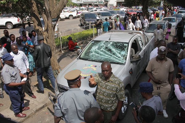 Passers-by and police look at Zanu-PF Harare Province political commissar Shadreck Mayamombe's branded vehicle which was stoned by #Tajamuka members protesting the police clampdown on forex dealers in Harare (Picture by Innocent Makawa)