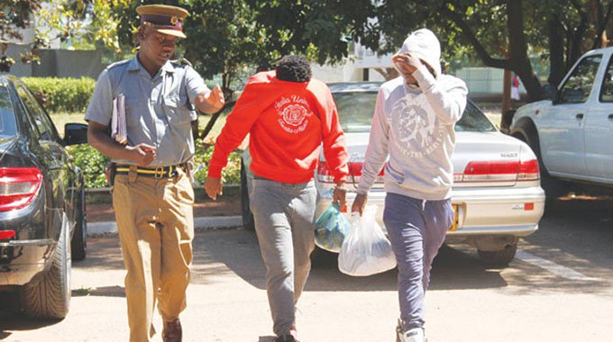 Zimbabwe international Achford Gutu (left) hides his head in shame as he is escorted into the Harare Magistrates’ Court together with his teammate Method Mwanjali in April 2016
