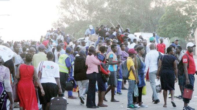 Commuters wait for transport as others (background) scramble onto trucks along Khami Road in Bulawayo yesterday